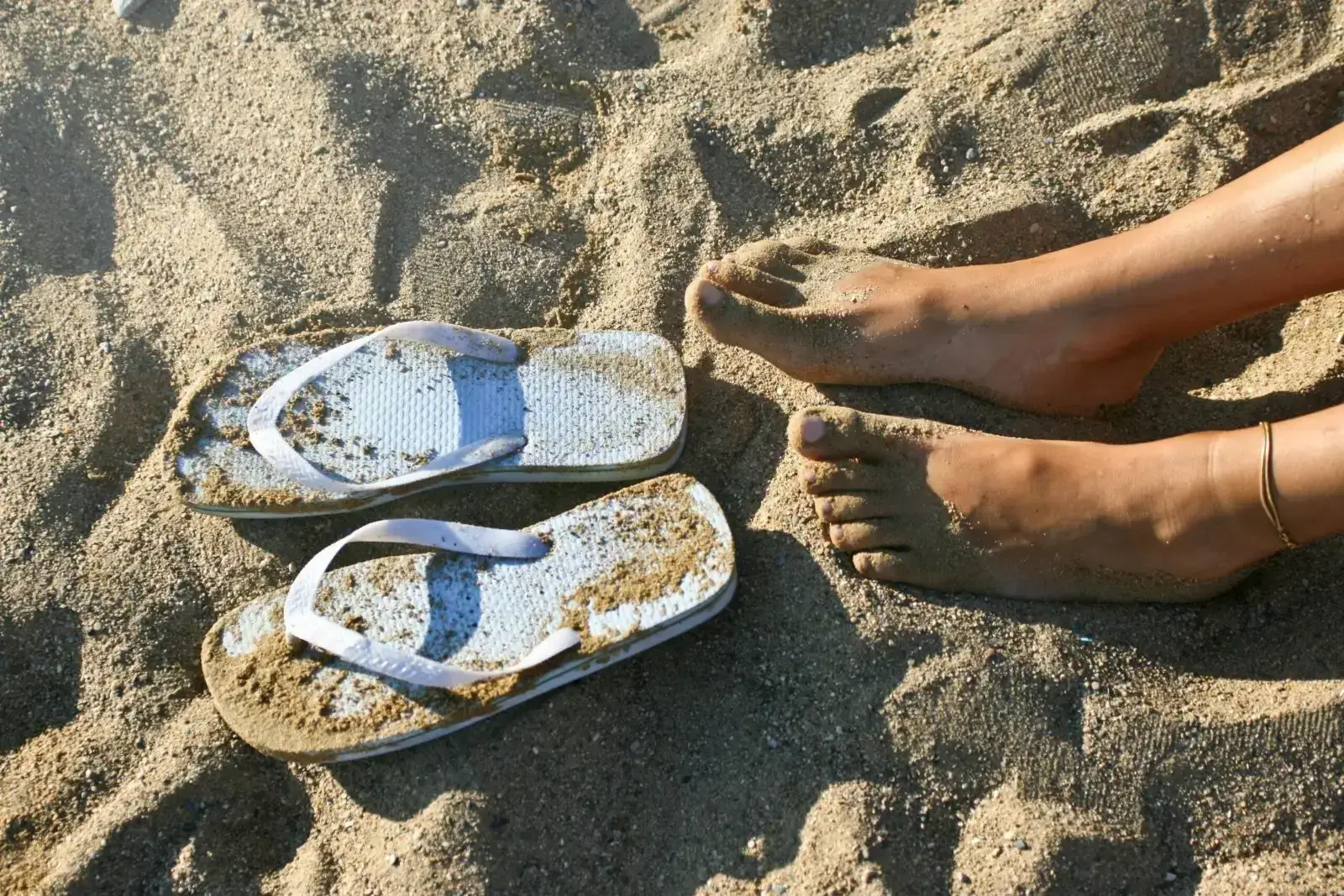 Casual sandals resting on a sunlit beach with ocean waves in the background, ideal for summer vacation themes.
